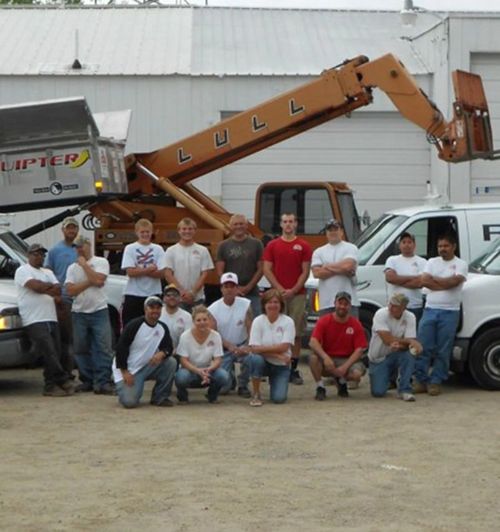 Group of workers posing in front of a raised orange boom lift and white van in a work yard
