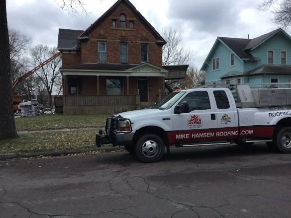 White roofing company pickup truck parked on a residential street in front of a brick house