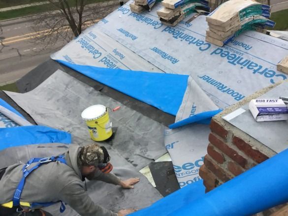 Worker installing blue tarp roofing on a flat roof near a brick chimney