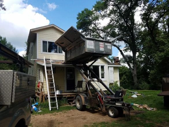 House being lifted by a crane during renovation, with ladders and a trailer in the yard.