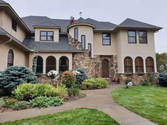 Large beige stucco house with arched windows, stone accents, and a landscaped front yard
