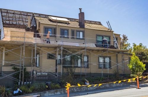 House under renovation with scaffolding and workers on the roof and balcony