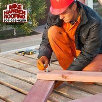 Worker in orange overalls measuring wood on a deck with a tape measure and pencil