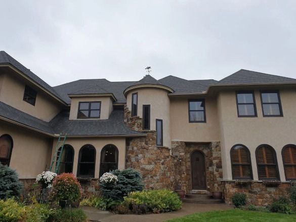 Large beige two-story house with stone accents, arched windows, and a landscaped front yard