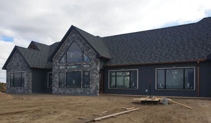 Modern dark-gray house exterior under construction with unfinished yard and large front windows