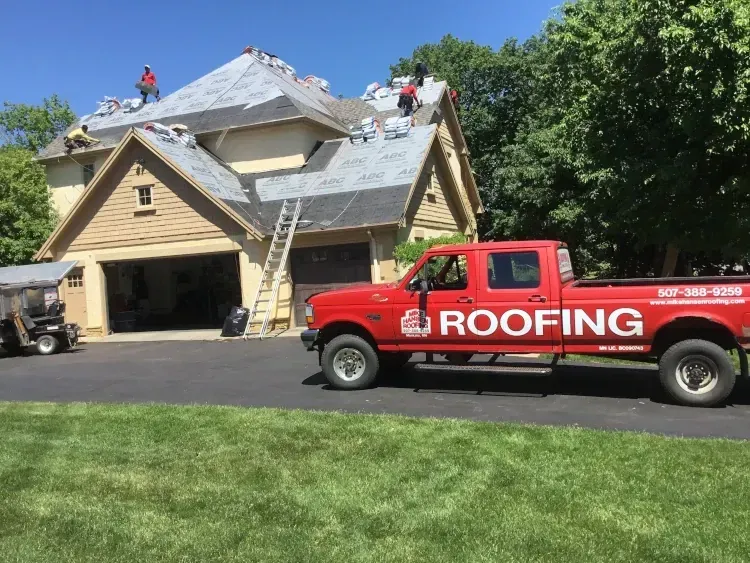 Roofers working on a tan house with ladder and red roofing truck in driveway