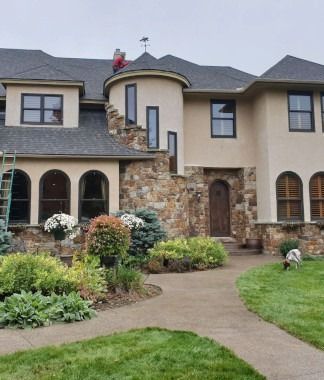 Large beige house with stone accents, arched windows, and a landscaped front garden with a curved walkway