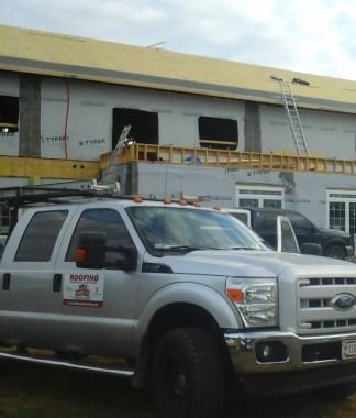 Silver work truck parked outside a building under construction with a ladder on the roof.