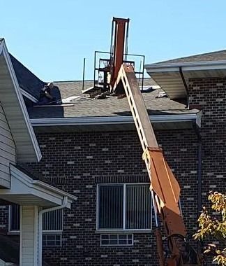 Workers using a bucket lift to repair a roof on a brick house