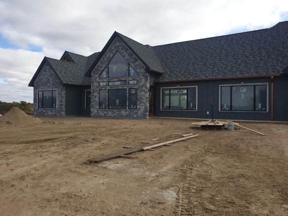 Newly built dark gray house with stone facade on a dirt lot under an overcast sky
