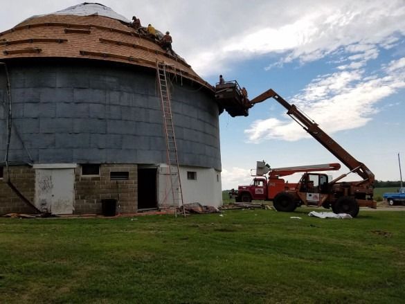 Workers use a lift to repair the roof of a large round silo on a farm.