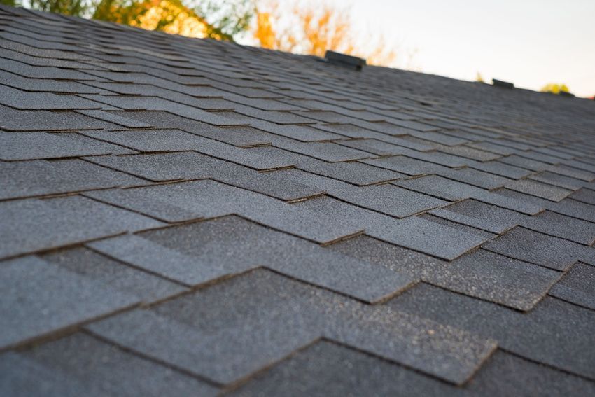 Gray asphalt roof shingles with a rooftop vent against a warm sky