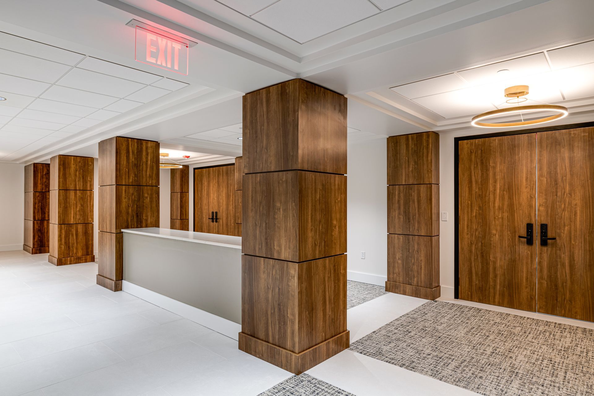 A hallway with wooden columns and a red exit sign.