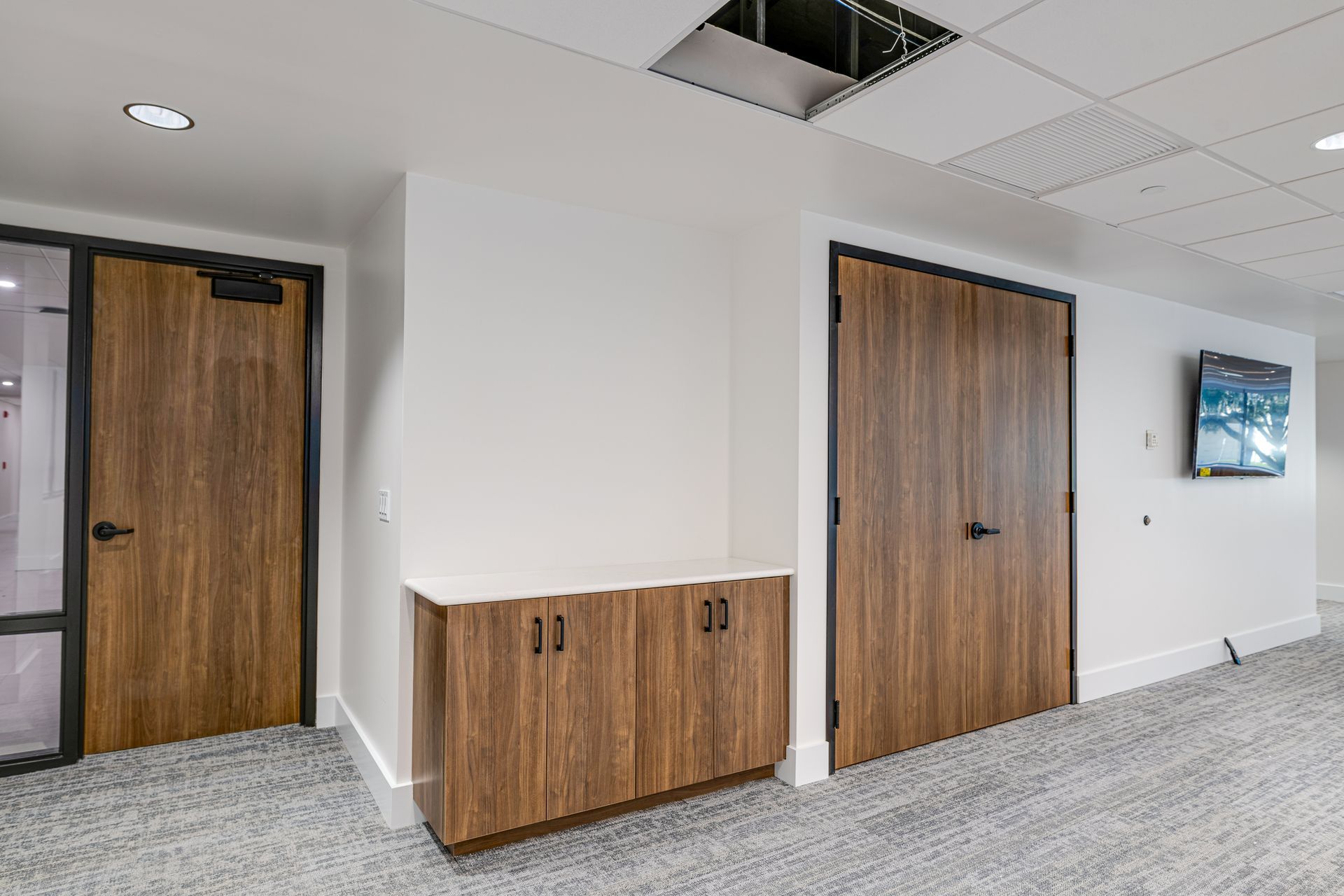 A hallway with wooden doors and cabinets and a television on the wall.