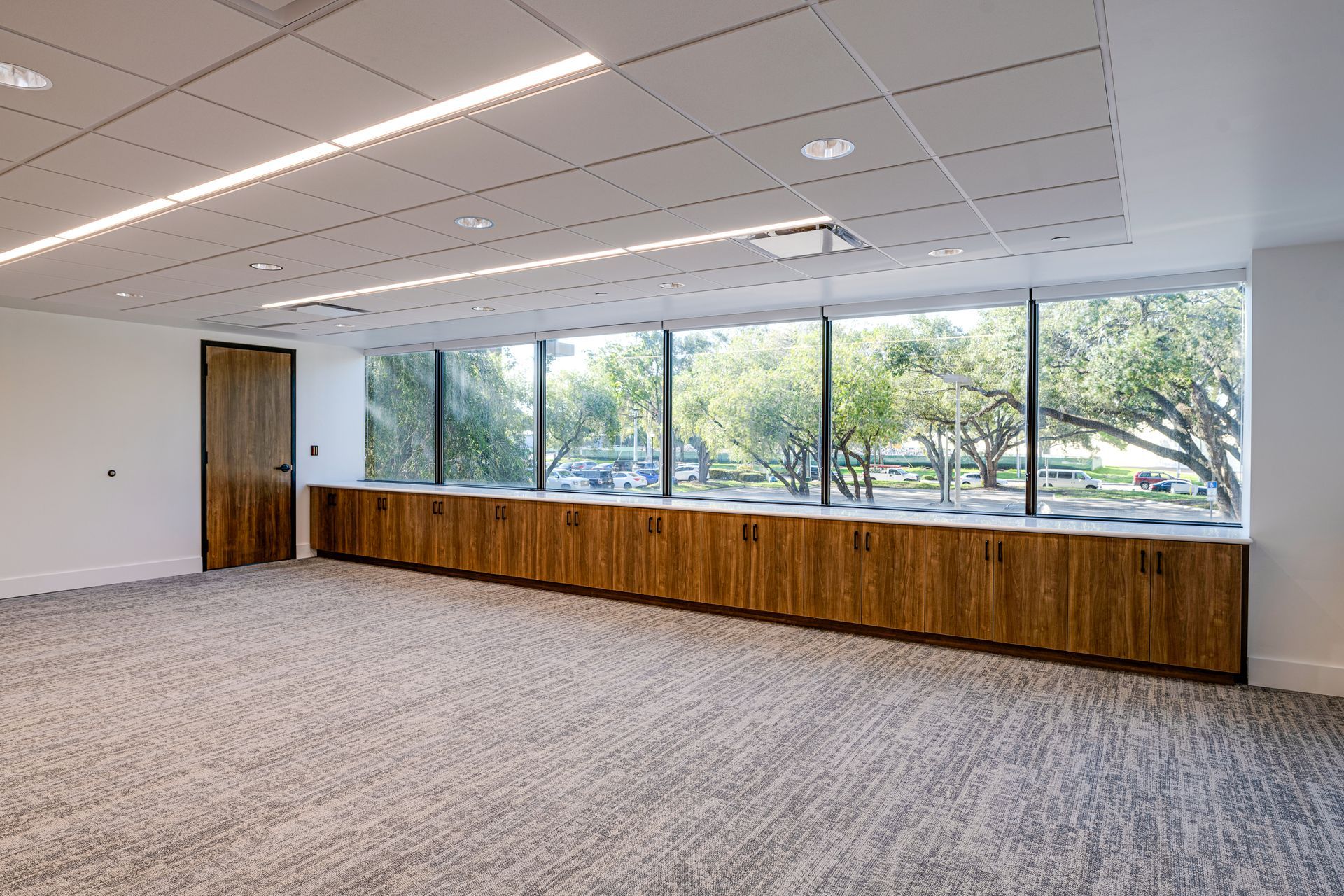 A large empty room with a lot of windows and wooden cabinets.