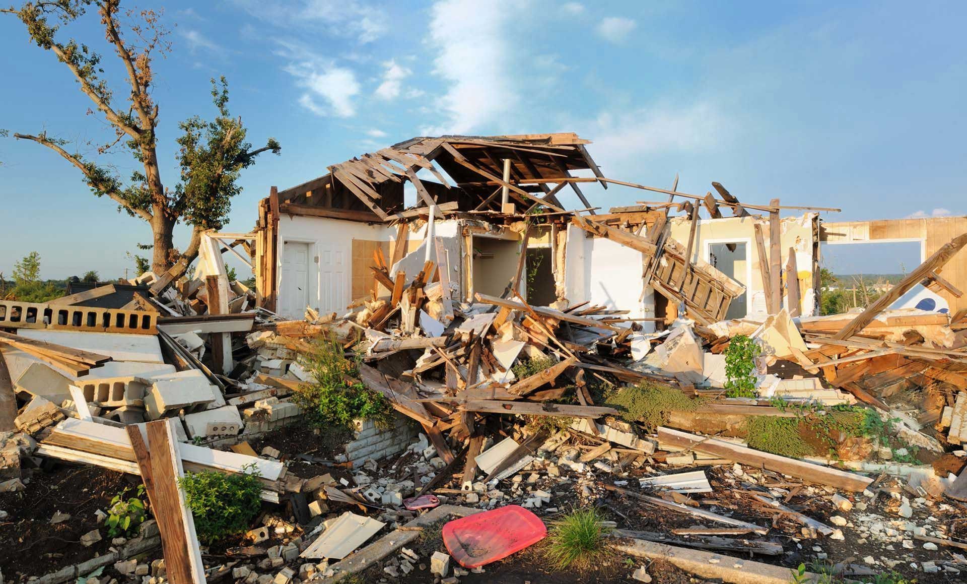 Damaged house, debris scattered; blue sky visible.