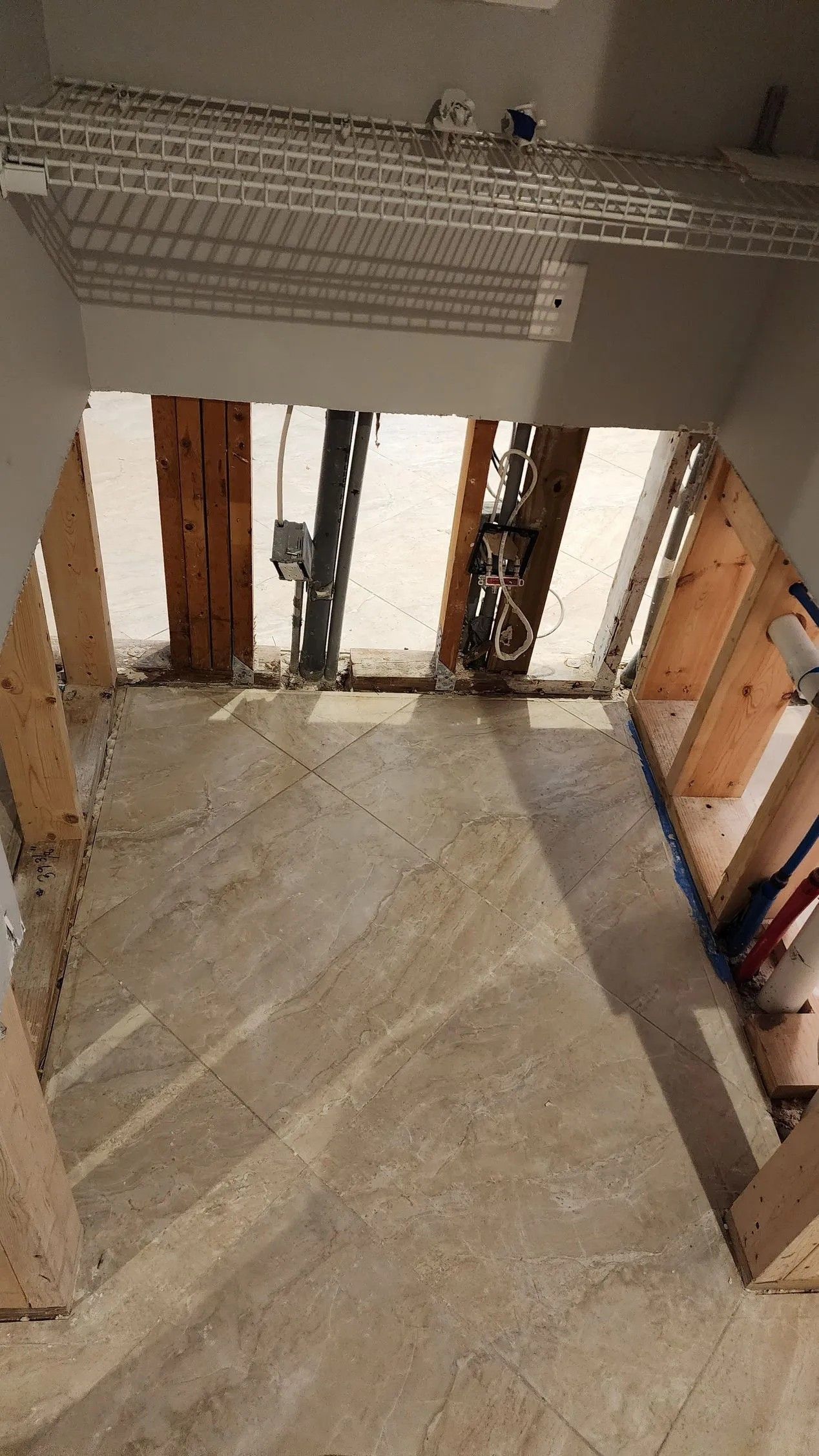 Framed opening in concrete floor, wooden beams, exposed wiring and pipes.