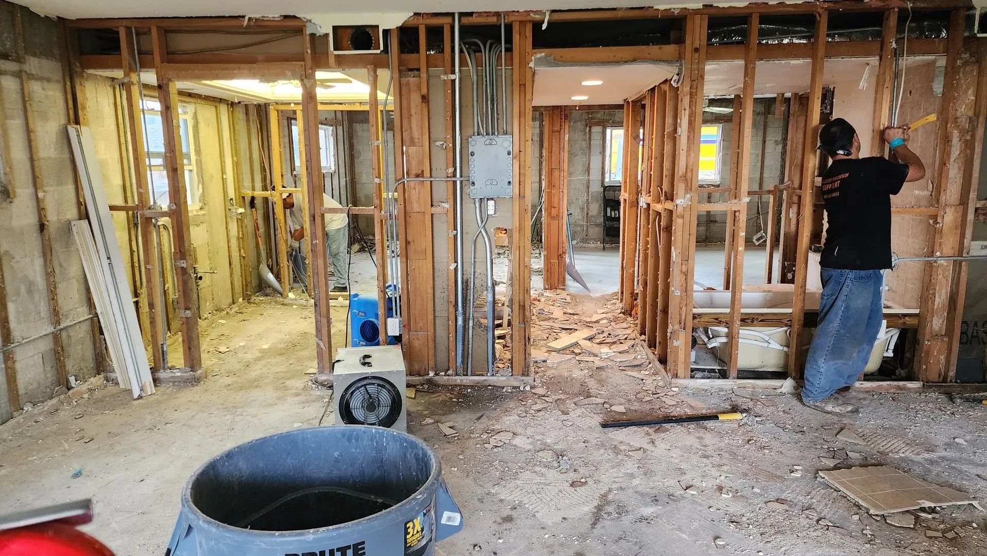 Interior demolition in progress. Person working, exposed wooden studs, debris on floor.