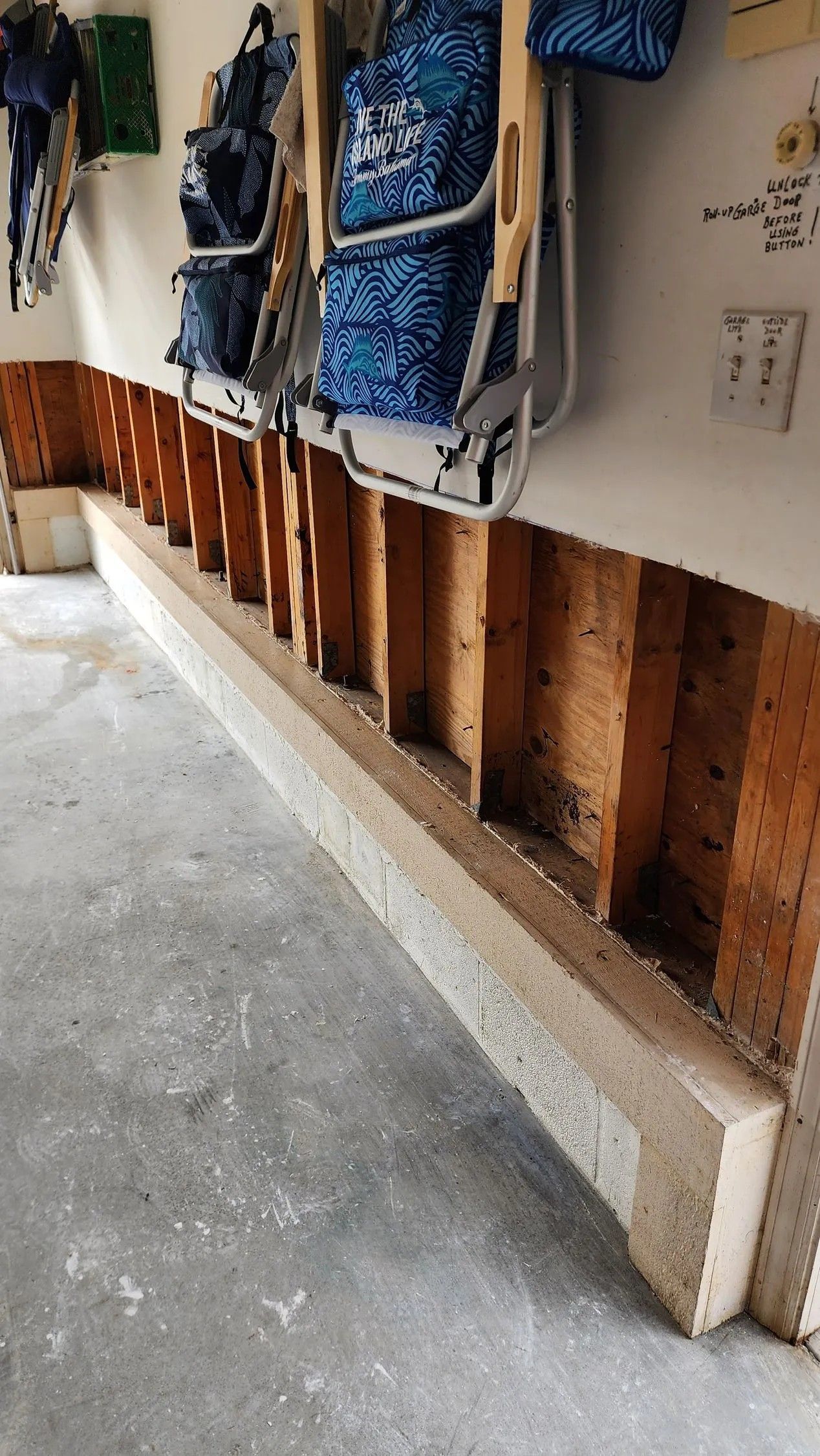 Wall partially opened, revealing wooden studs, with concrete base. Items hanging above.