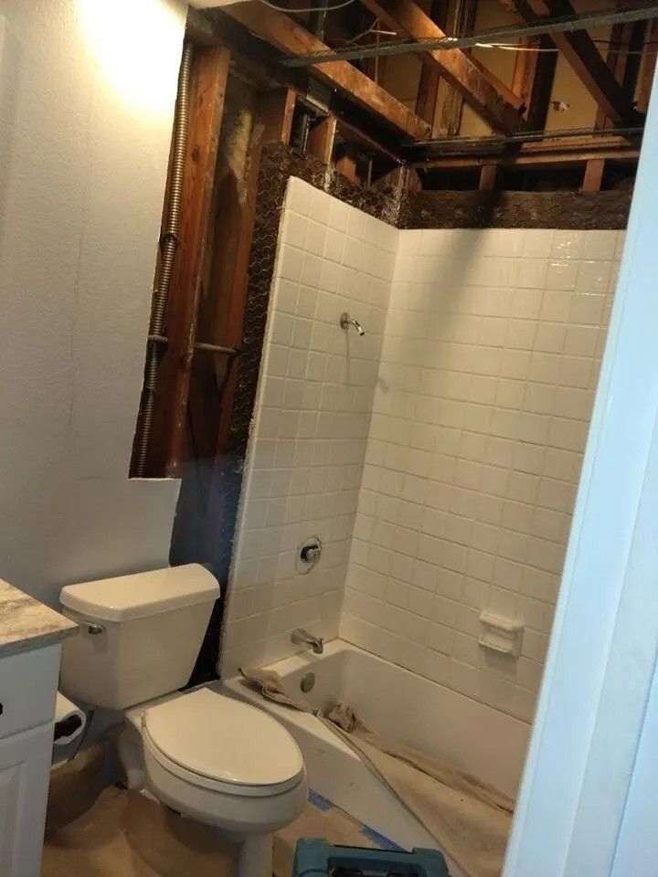 Bathroom under construction, showing a toilet and tiled shower stall with exposed wall framing.