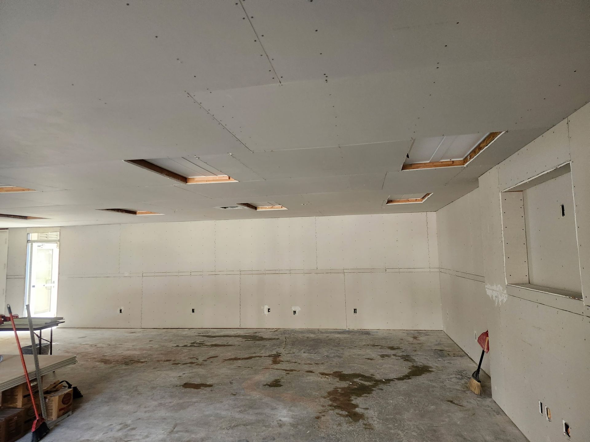 Interior of a room under construction with unfinished drywall on ceiling and walls. Holes in the ceiling. Concrete floor.