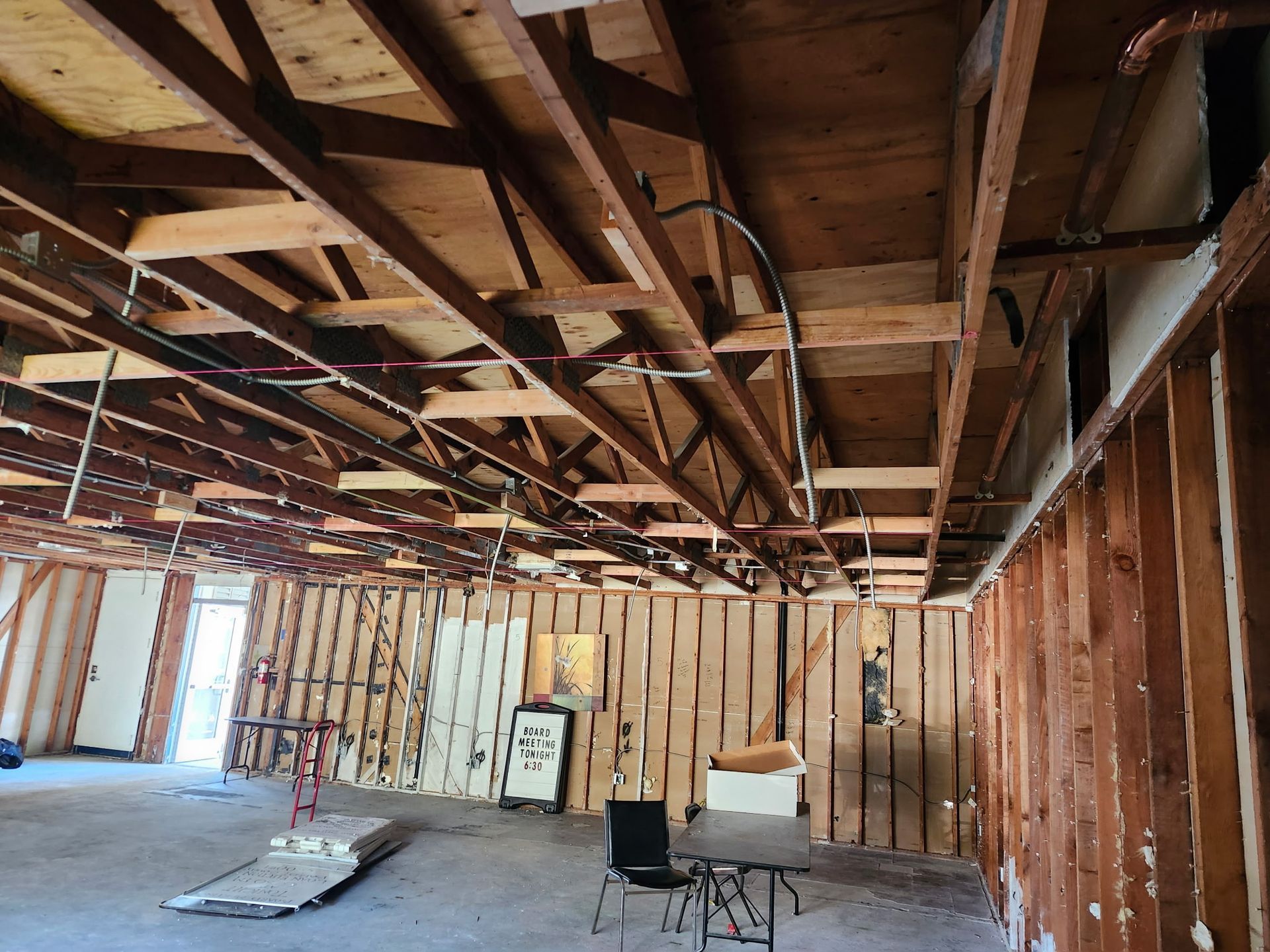Interior space undergoing renovation, exposed ceiling beams, studs, and concrete floor.