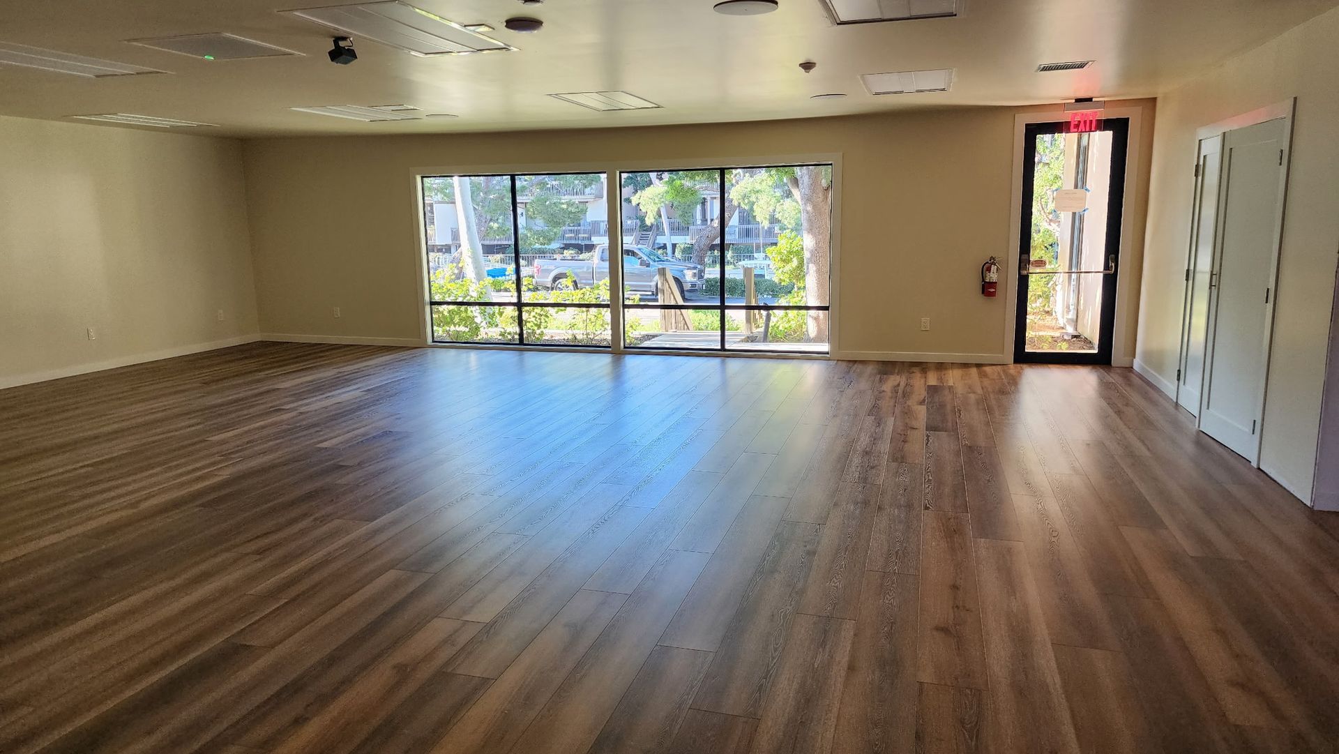 Empty room with wood floors, large window, and exit door.