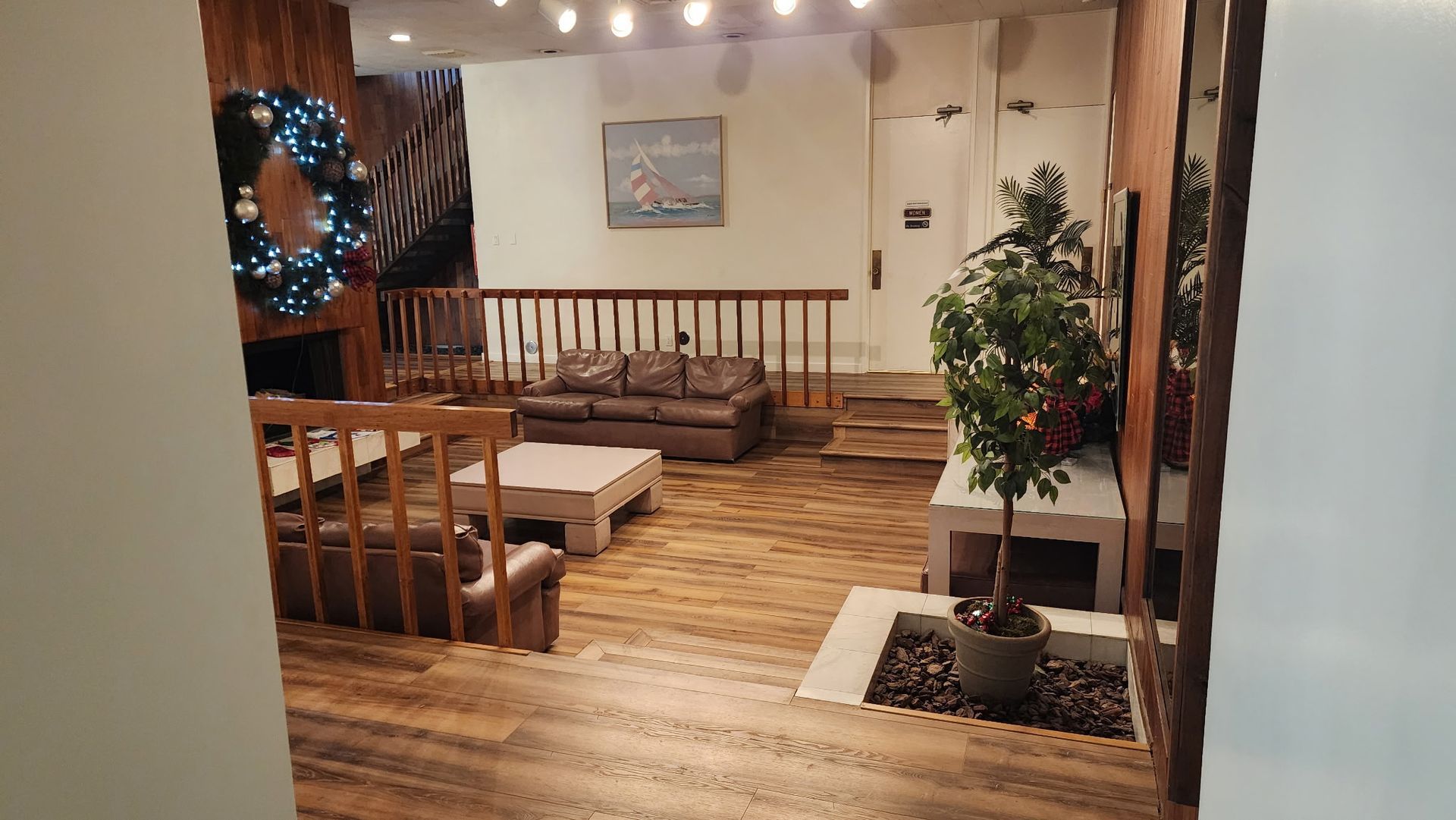Cozy living area with sofas, fireplace, and Christmas wreath. Wooden floors and accent walls.