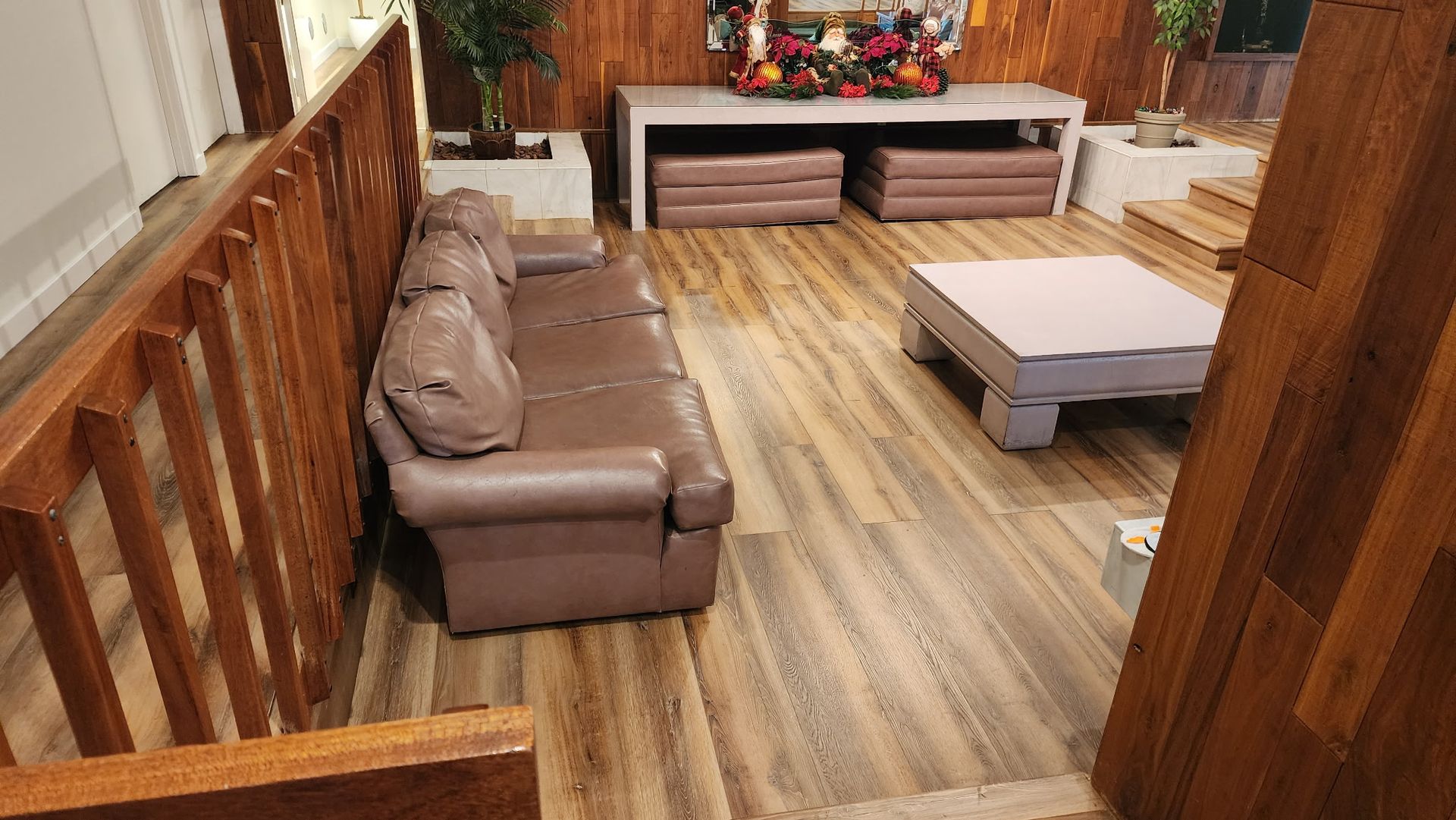Living room with brown leather sofa, wooden floor and stairs, light blue coffee table, and wood paneling.
