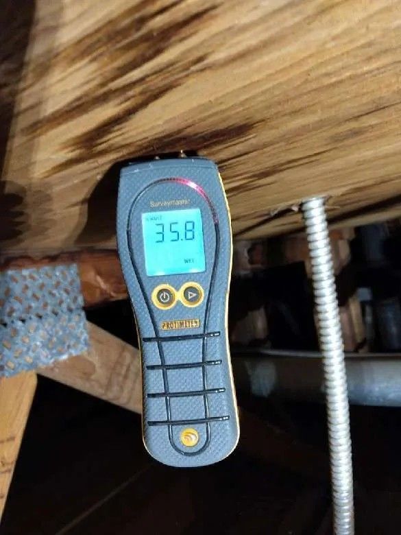 Moisture meter on a wooden beam, reading 35.8. Dark, likely in an attic or crawlspace.