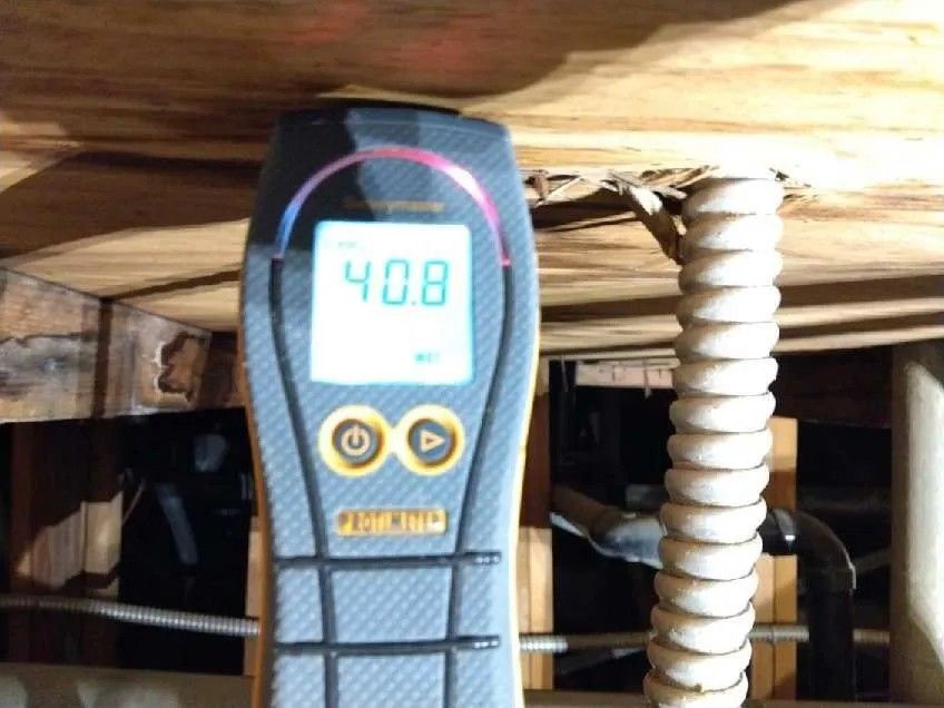 A moisture meter displaying 40.8 rests on wood in a crawl space.