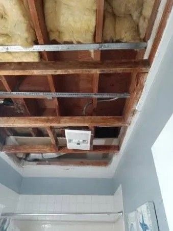 Ceiling partially opened, exposing beams, insulation, wiring, and a vent in a bathroom.