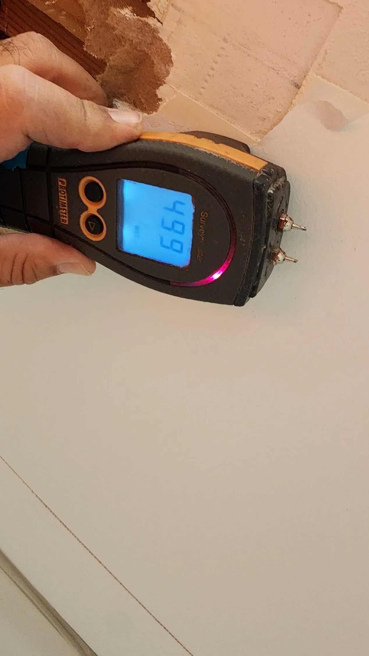 Person holding a moisture meter against a white wall, reading 46.9.