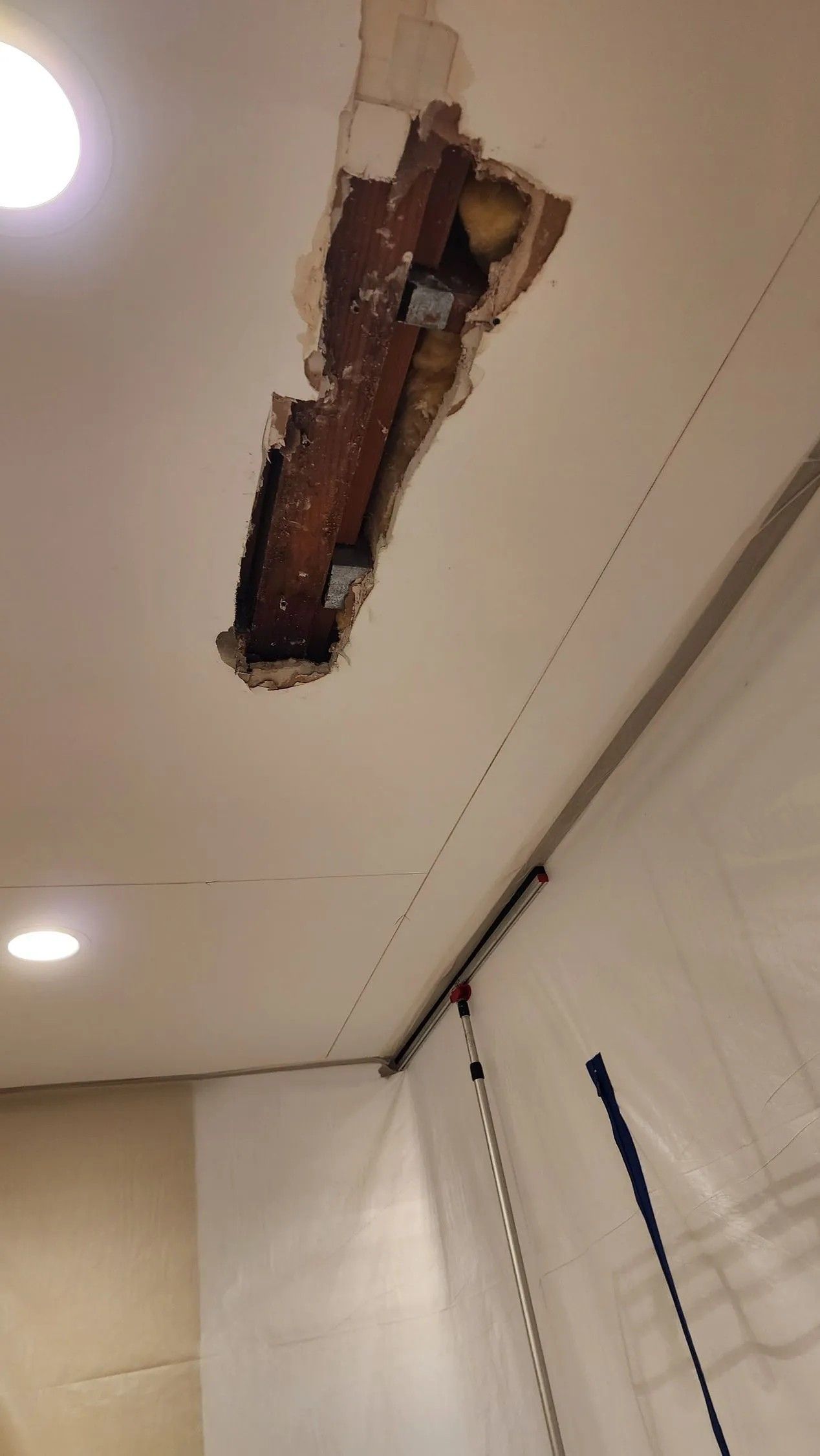 Ceiling damage with a hole exposing wood beams and a crack along the wall.