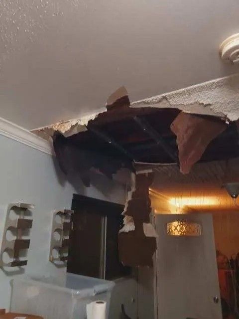 Damaged ceiling with a large hole. Brown debris hangs down. White and tan walls.