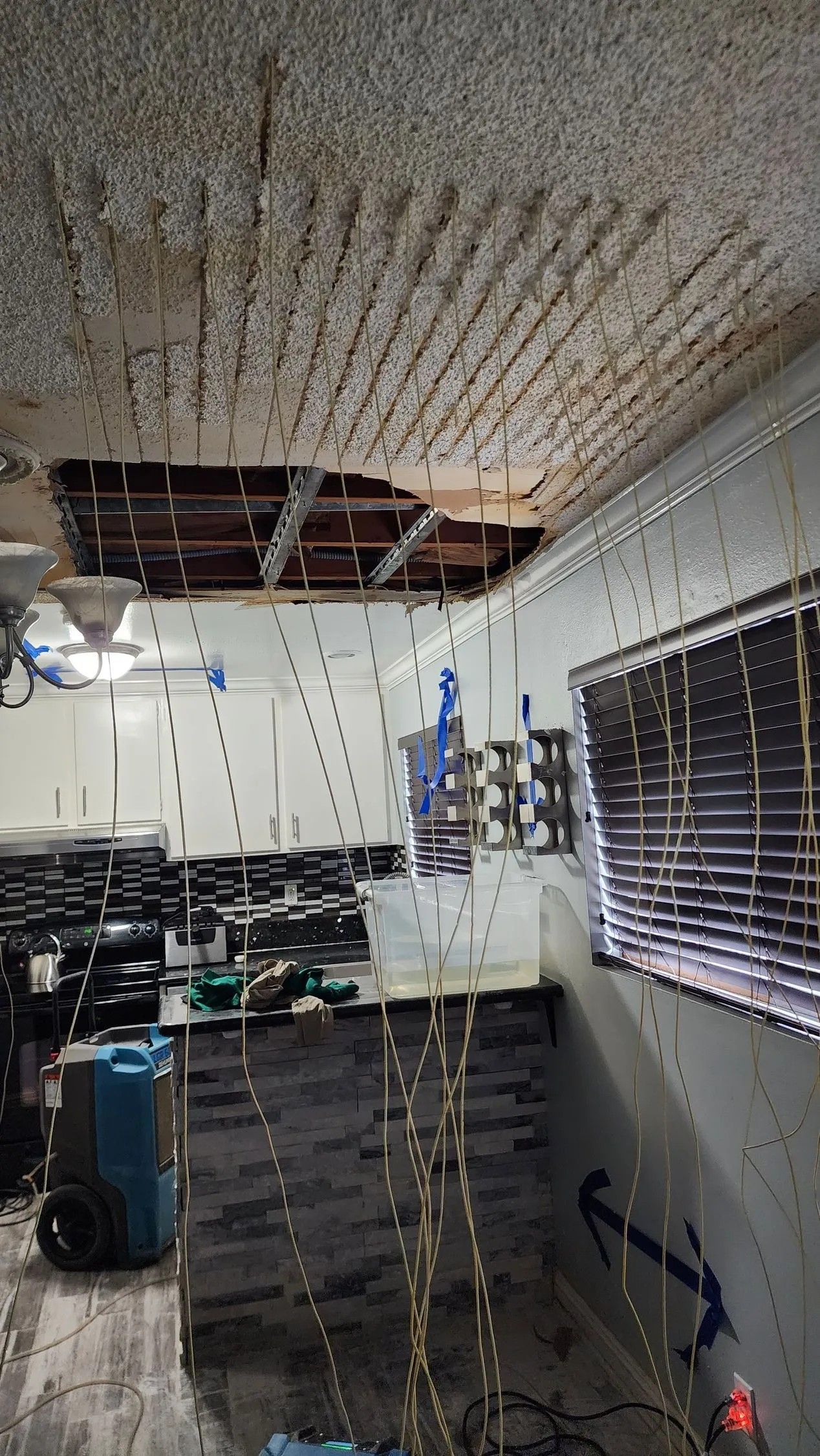 Interior view of a room with ceiling damage and remediation equipment; blue arrows point.