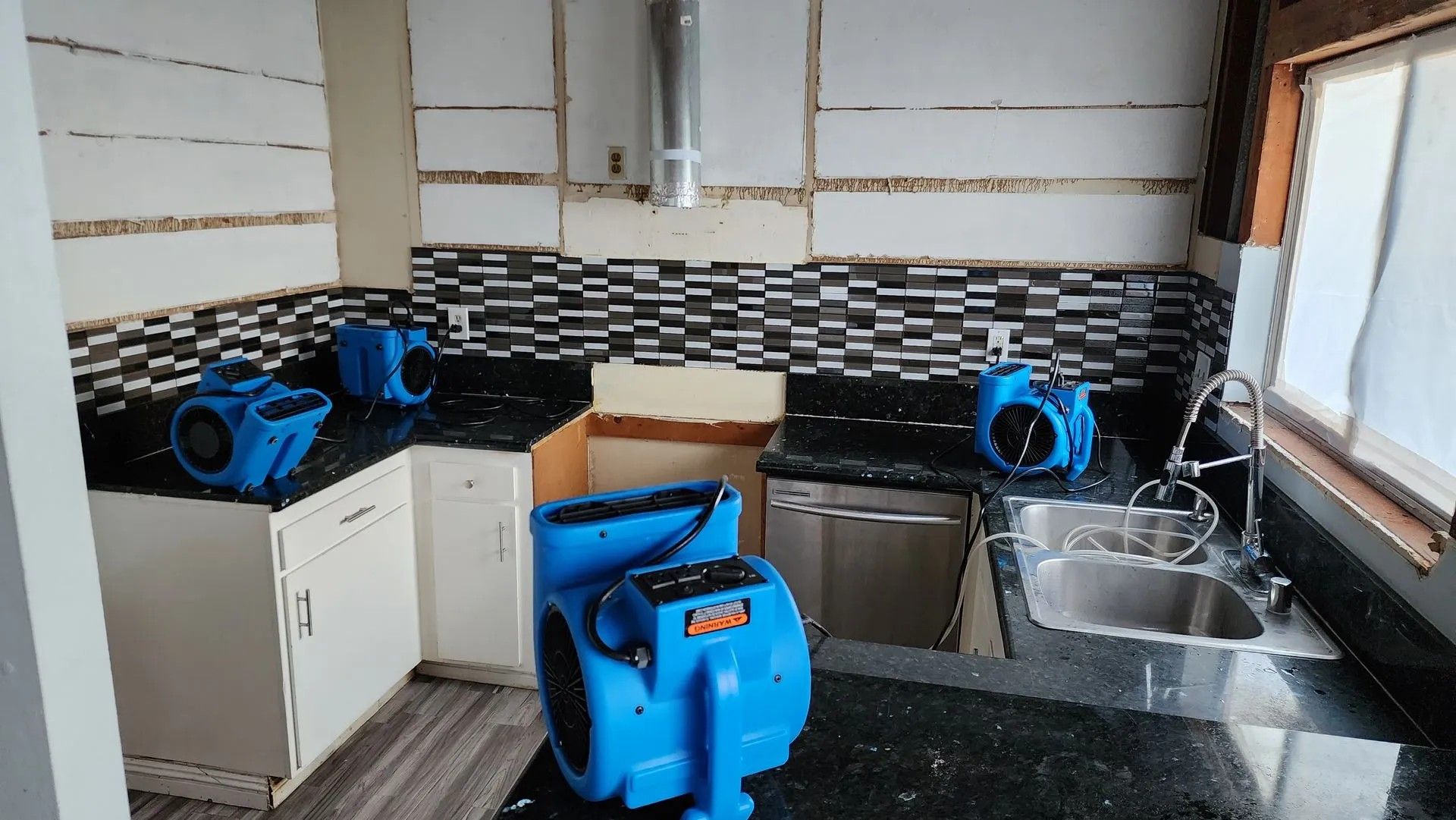 A kitchen with several blue air movers, black countertops, and a black and white tile backsplash.