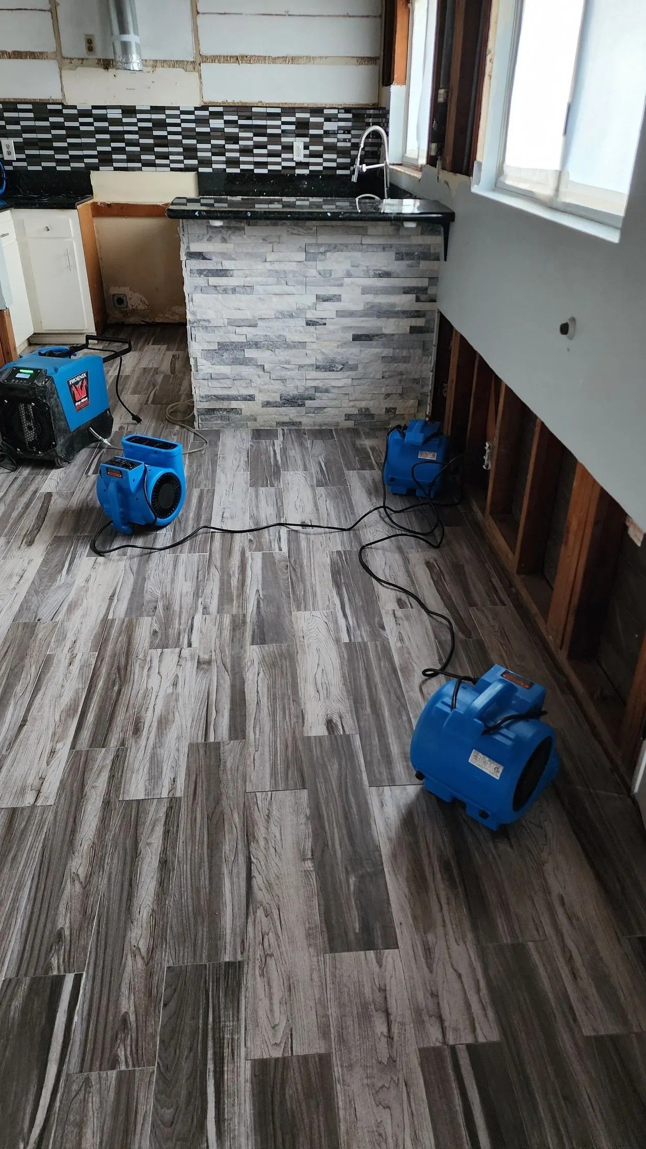Room with water damage, drying equipment deployed on flooring; exposed wall studs.