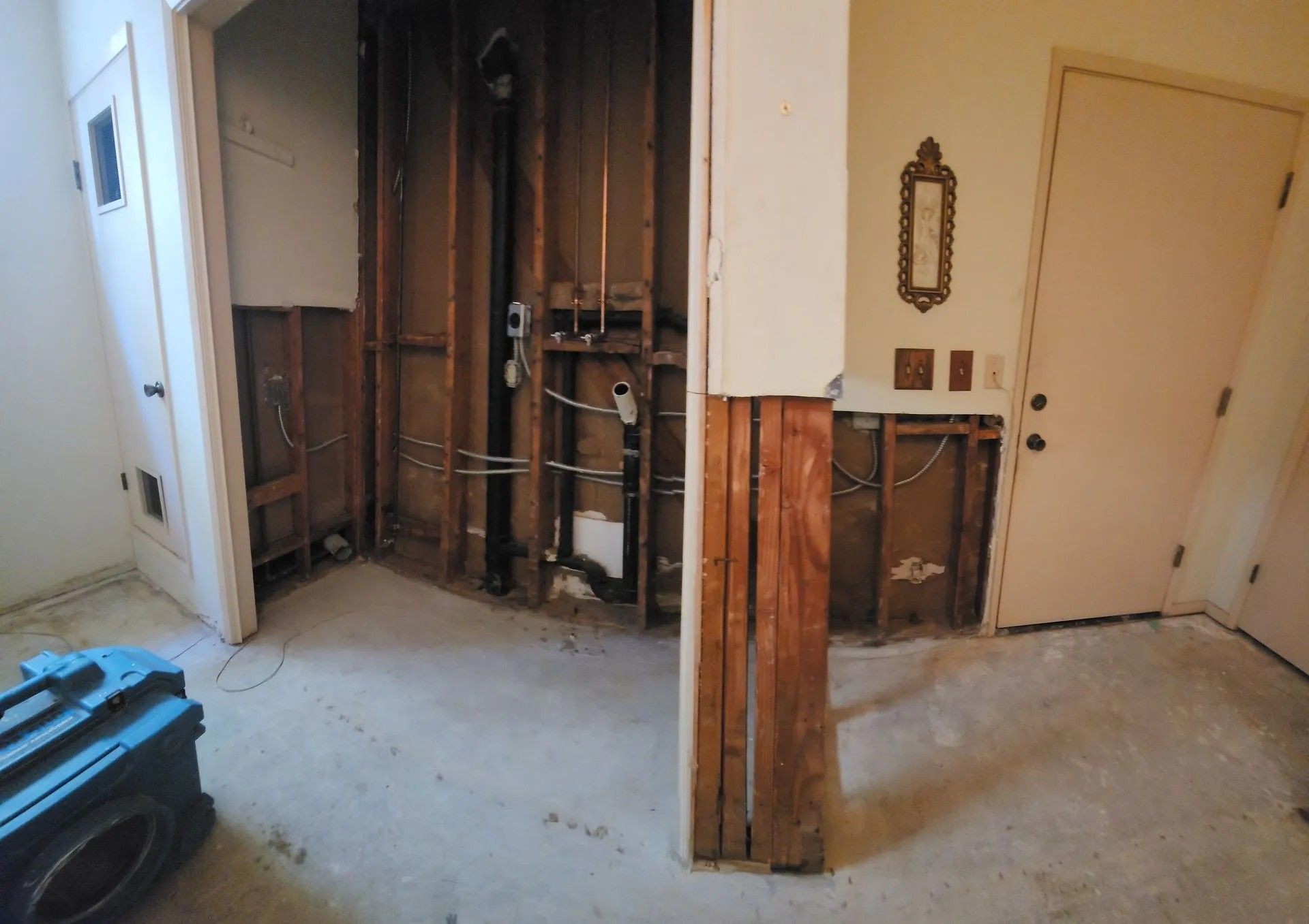 Interior room under construction, walls exposed, with wiring and plumbing visible. Beige and brown tones dominate.