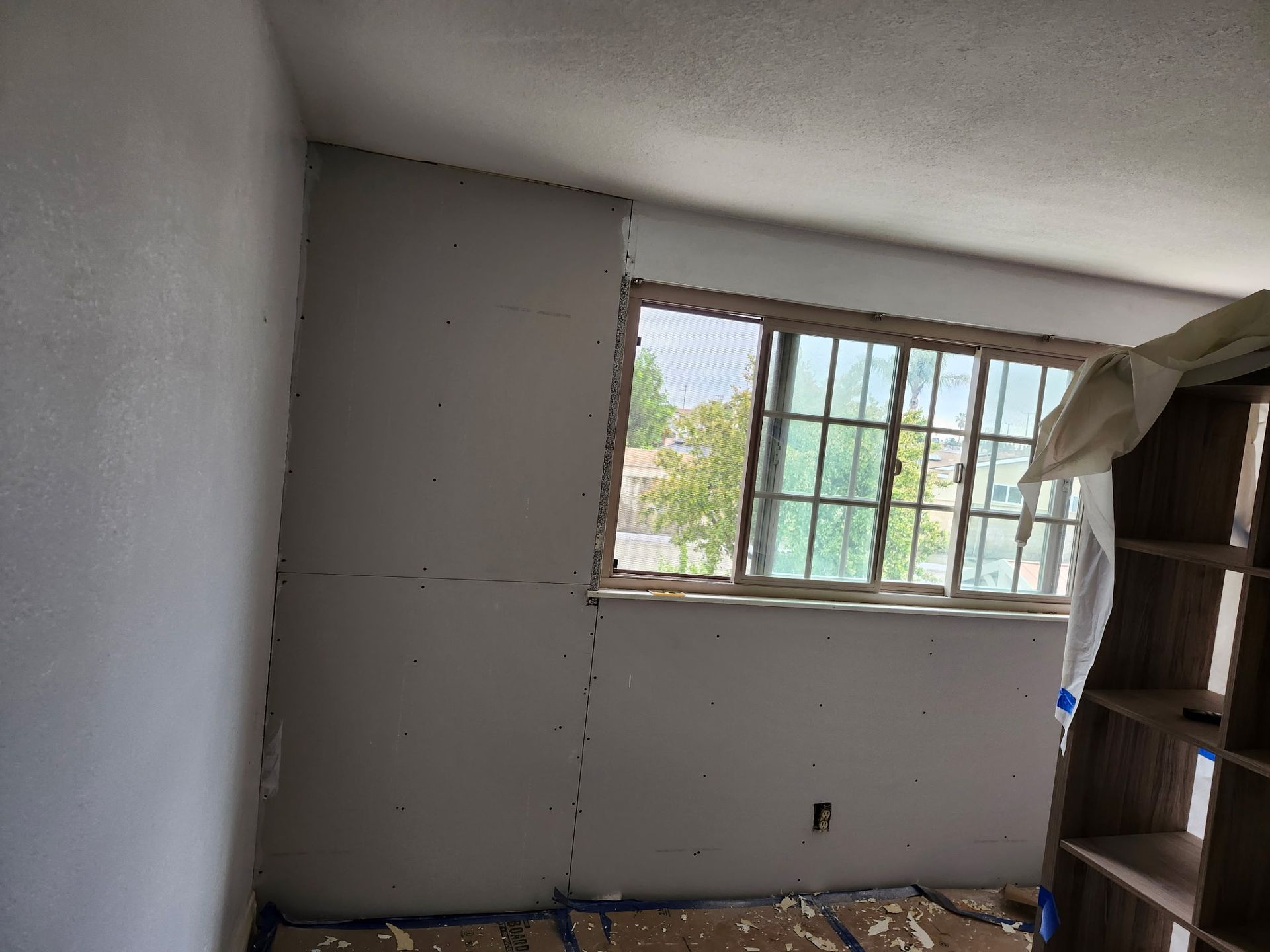 Room with window under construction; drywall installed, unfinished walls, and cardboard on floor.