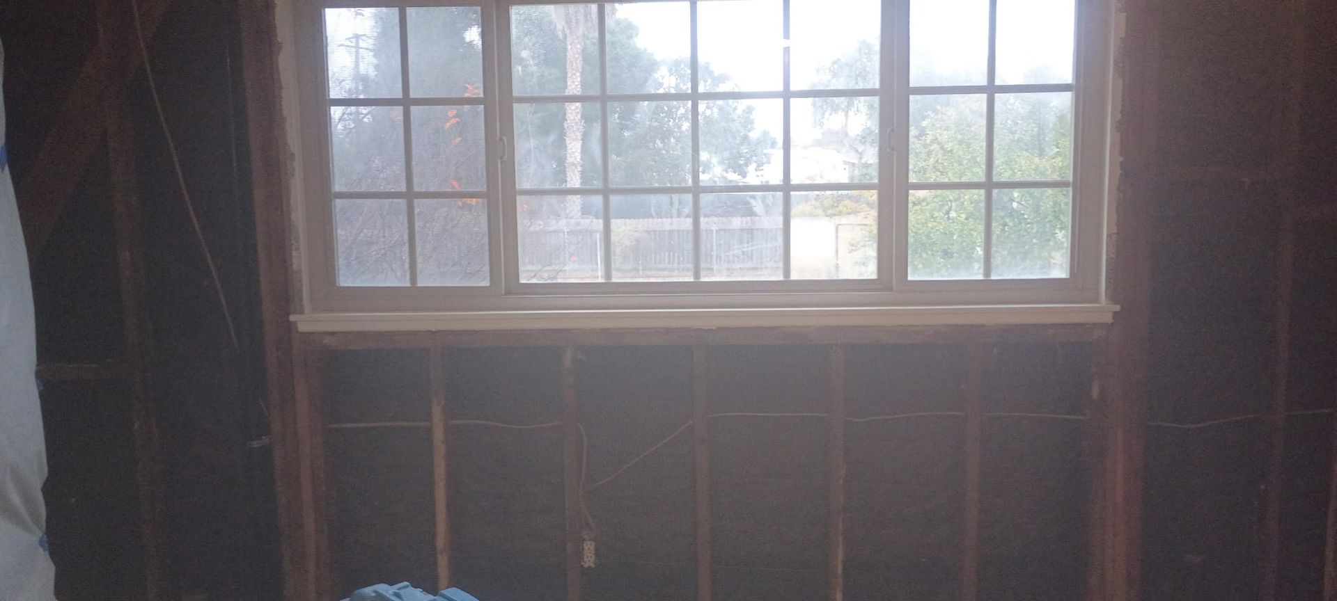 Window in a room with exposed wooden studs. Outside is visible through the window.