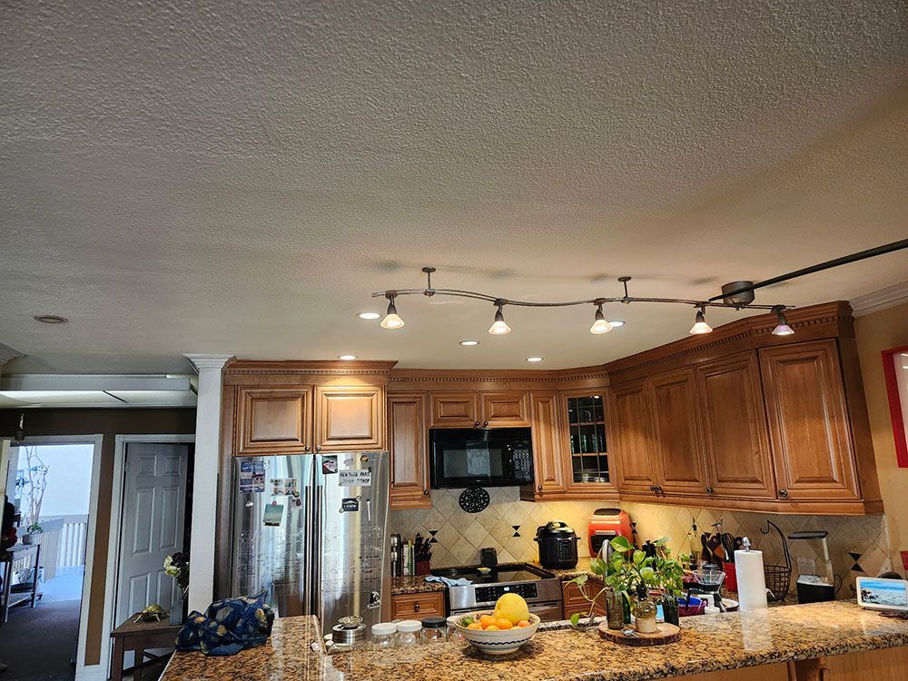 Kitchen with wooden cabinets, stainless fridge, countertop clutter, and ceiling track lights