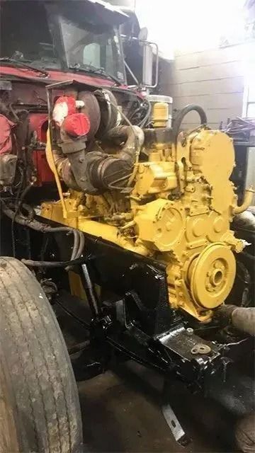 Yellow engine installed in a red truck, undergoing repair in a garage.