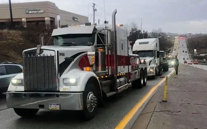 Three semi-trucks on the side of a road, one white with red stripes. Person walking.