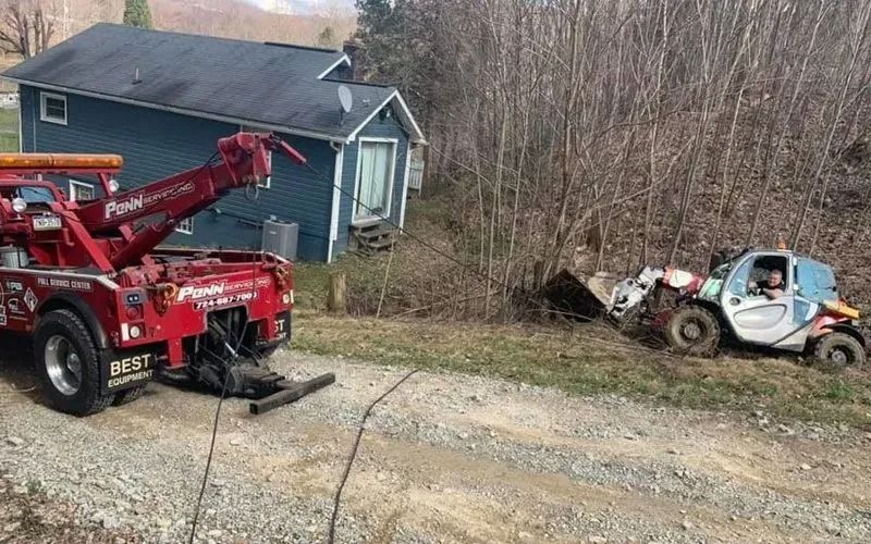 Red tow truck pulls a small vehicle from a ditch near a blue house.