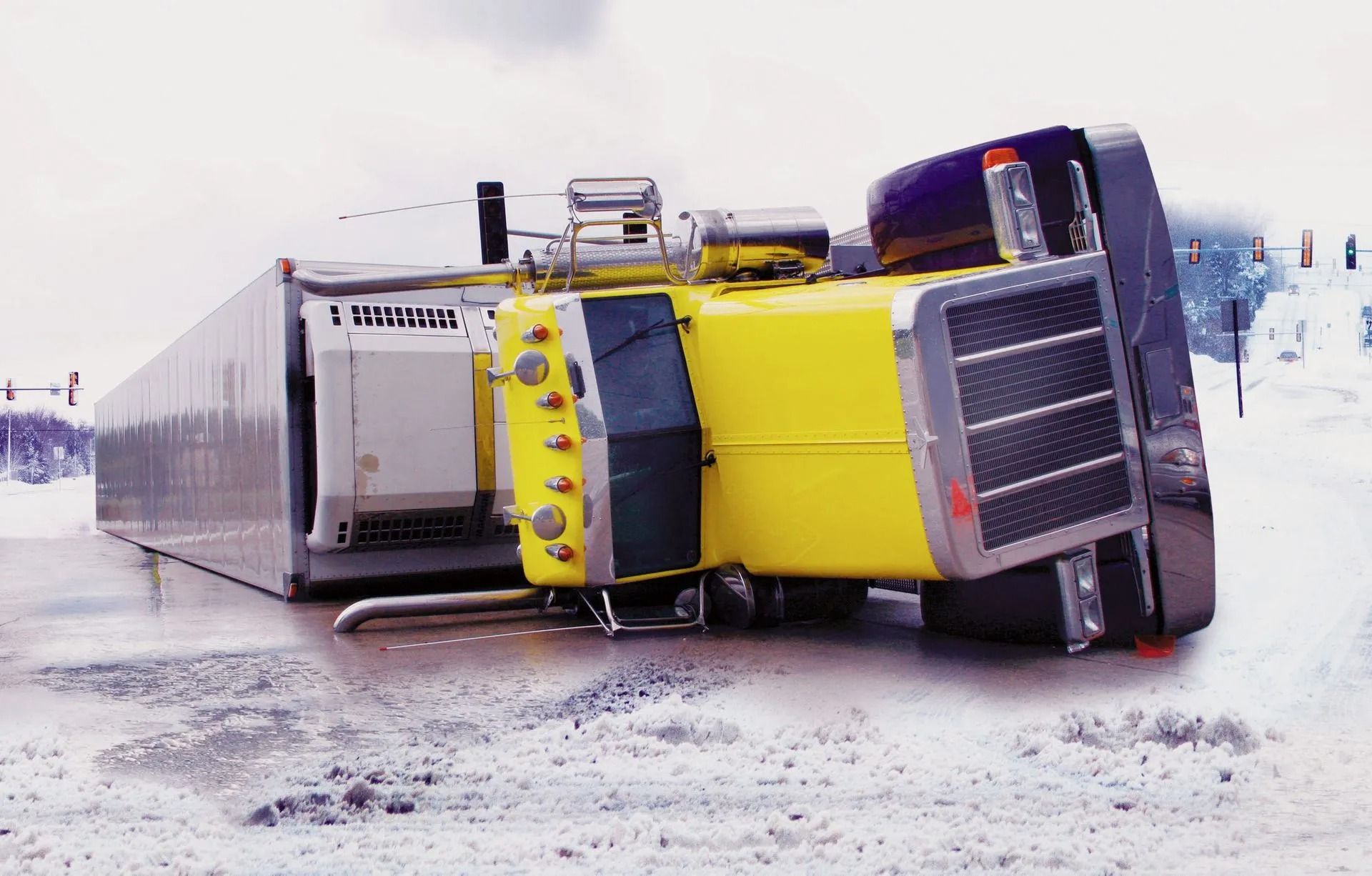 Yellow and black semi-truck overturned on a snowy road, trailer damaged.