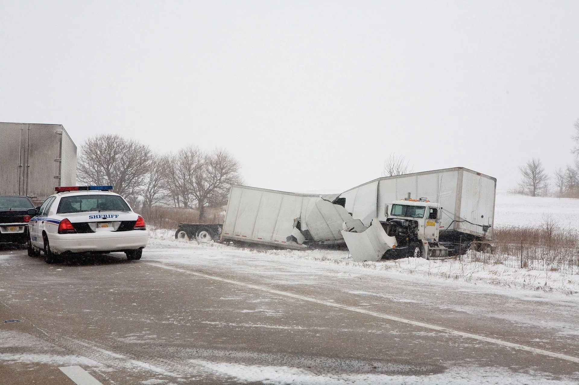 Semi-truck crash on snow-covered road; police car at scene.
