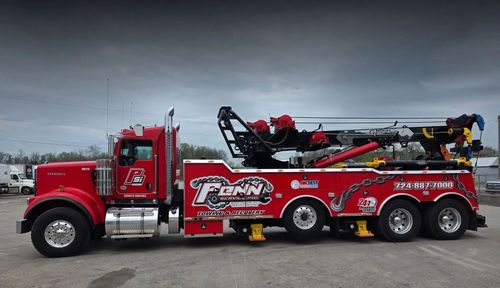 Red tow truck parked outdoors. Features logos, a large lifting arm, and a cloudy sky.