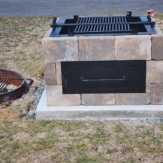 A grill made out of bricks is sitting next to a fire pit.