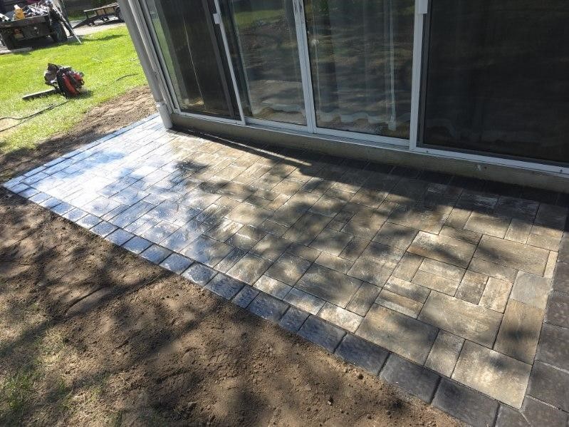 A patio with a sliding glass door is being built in front of a house.